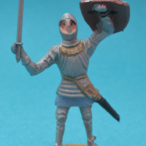 1213 Chevalier en armure, jambes parallèles, bras levés avec arme et bouclier, visière fermée.